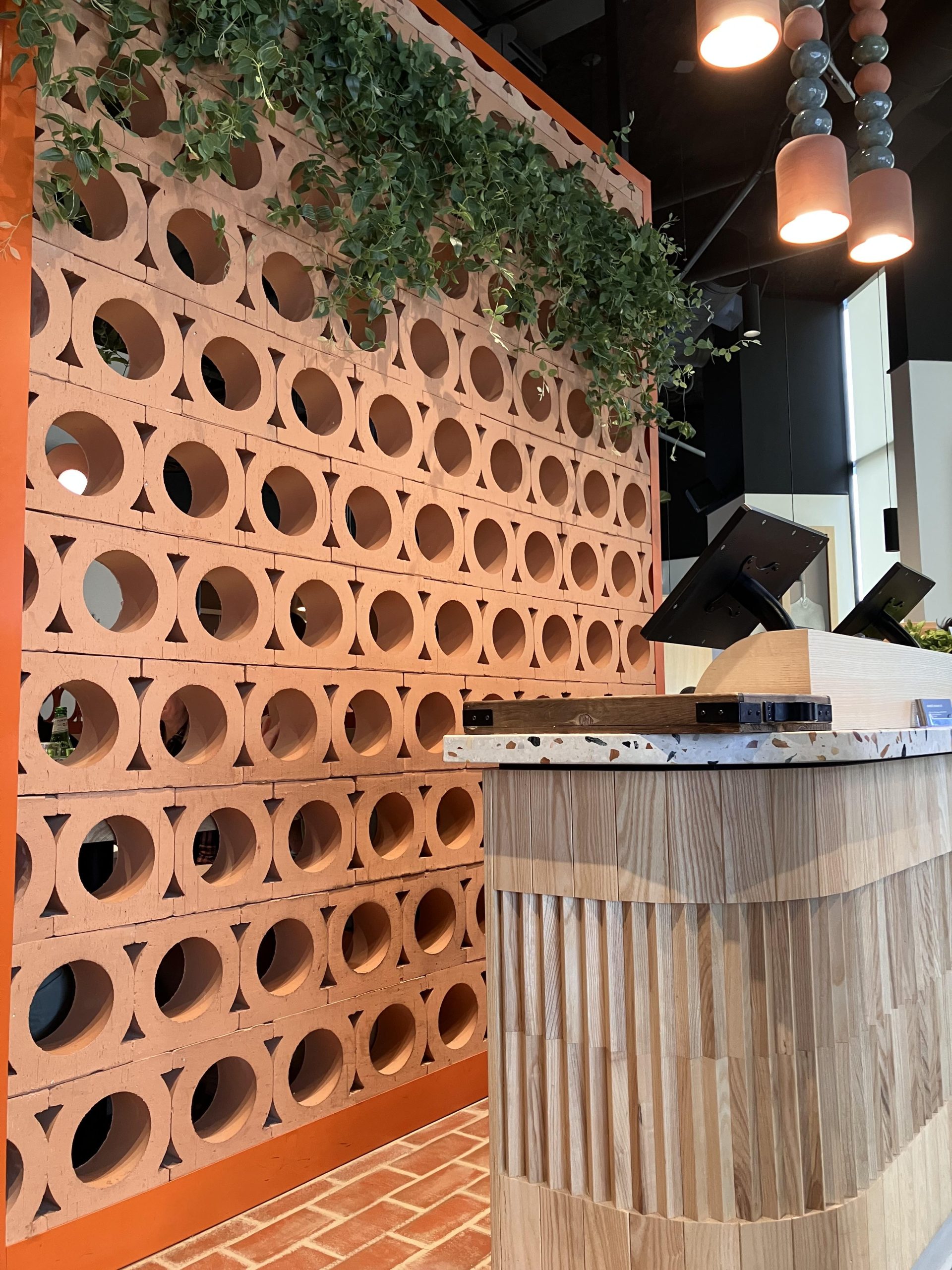 Terracotta-colored breeze blocks with circular openings and trailing greenery at Bardo Brant Restaurant.