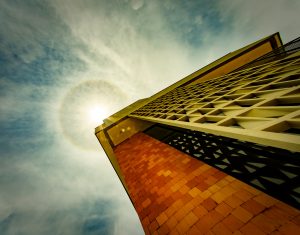 Sunlight breaking past a geometric breeze-block screen beside an orange brick wall.