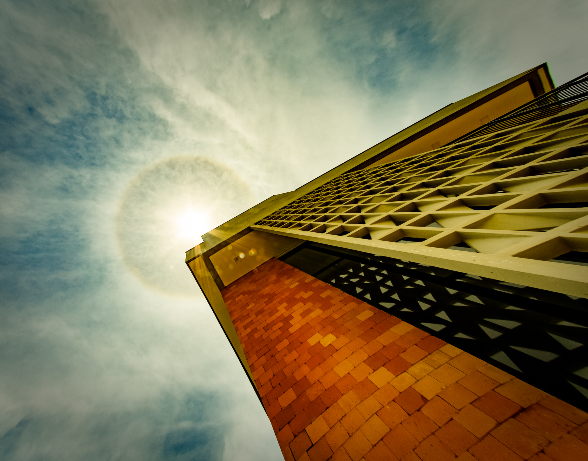 Sunlight breaking past a geometric breeze-block screen beside an orange brick wall.